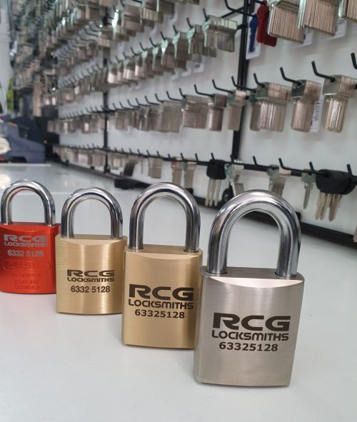 Four padlocks on the bench with the name RCG Locksmiths on each. A large amount of keys on a keyboard in the background.